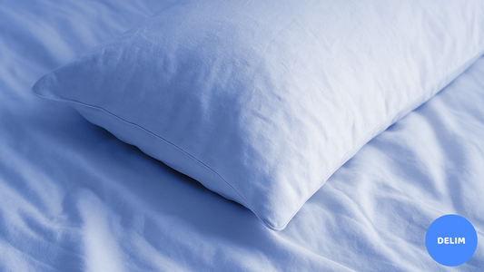 A close-up of a clean, cream-colored pillow resting on matching bedsheets, highlighting soft fabric texture and gentle folds in a cozy, well-lit bedroom setting.